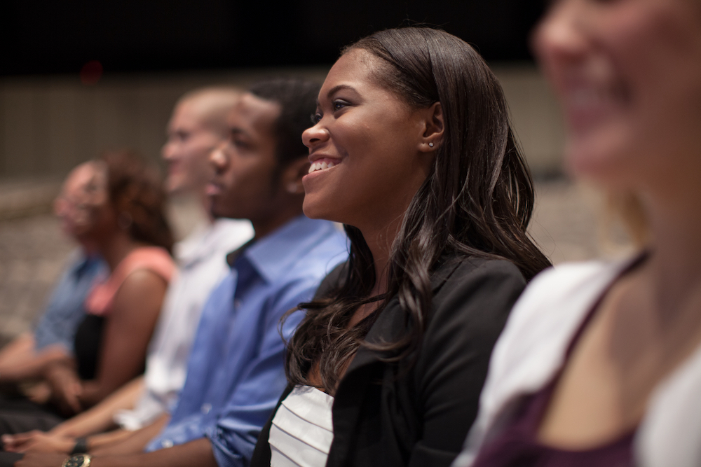 Woman smiling listening sitting next to a group of other people listening to a sermon.